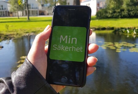 En hand håller i en iPhone. Skärmen visar vit text Min säkerhet på grön bakgrund.