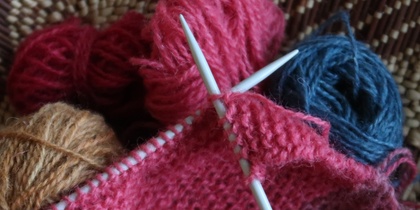 Närbild på stickning med rosa garn, stickor och garnnystan i olika färger.