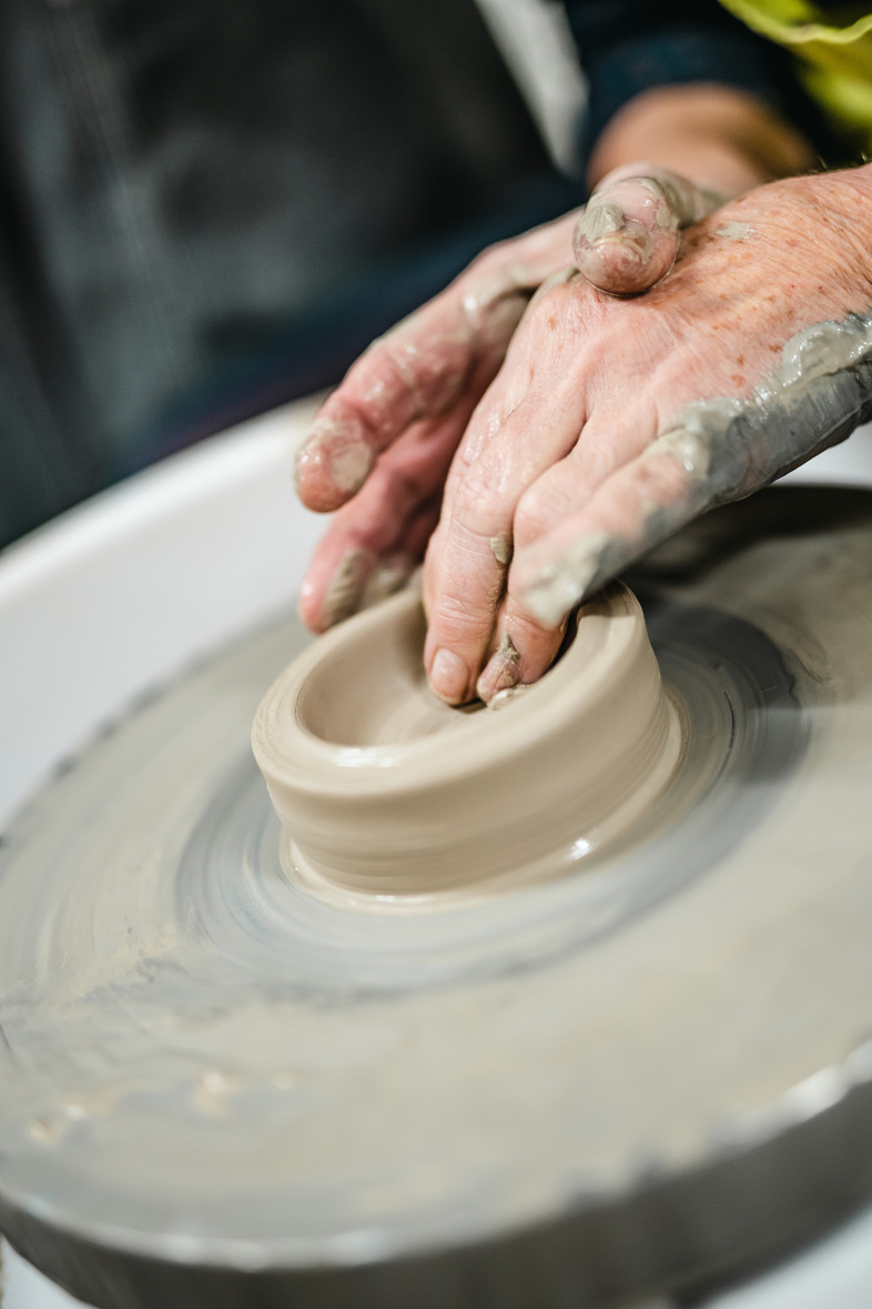 Två händer formar lera på en drejskiva under keramikarbete.