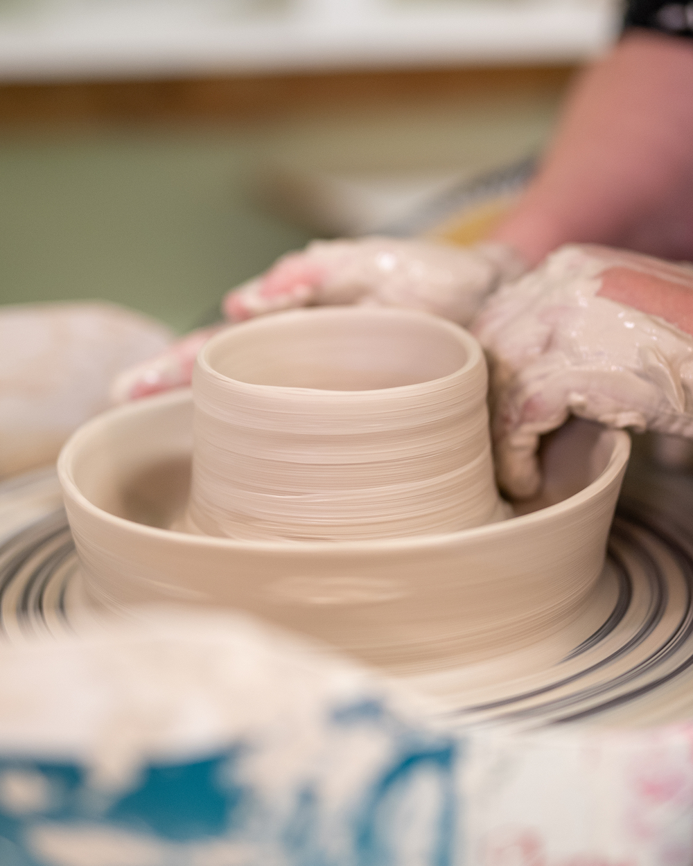 Närbild av händer som formar lera på en drejskiva under keramikarbete.