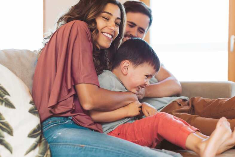 Två vuxna busar med ett barn i en beige soffa.