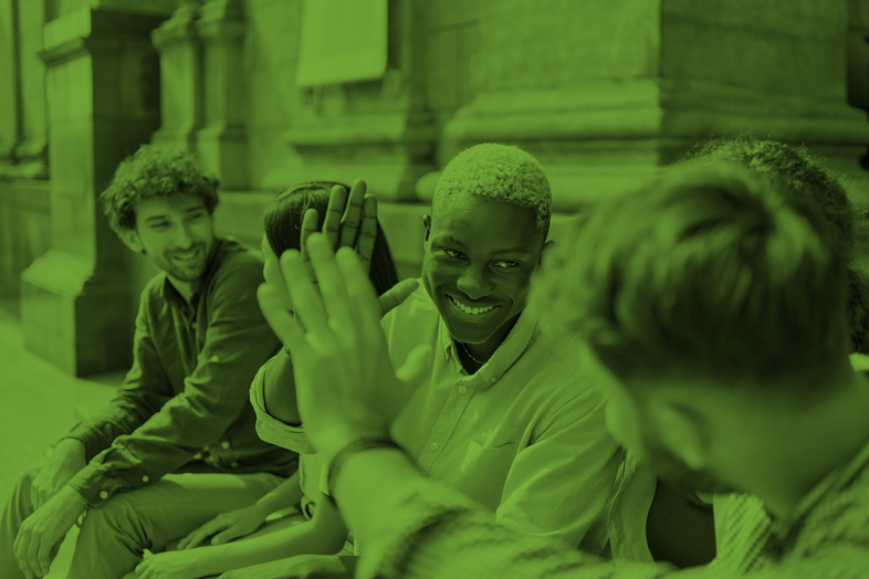 Fyra unga personer sitter utomhus, två av dem ger varandra en high five och ler.