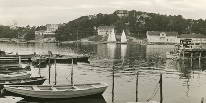 Svartvit bild av småbåtar vid en brygga i Stenungsund, med segelbåtar och hus i bakgrunden.