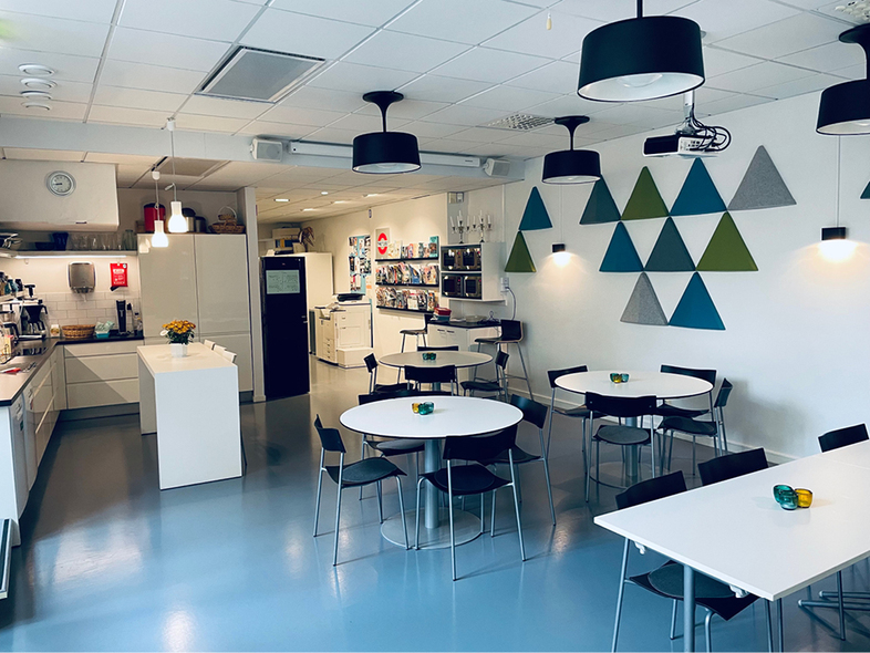 Ett modernt personalrum med runda bord, svarta stolar, kök och färgglada trianglar på väggen.