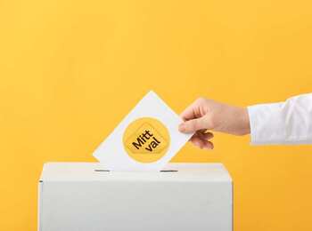 En hand lägger en röstsedel med texten 'Mitt val' i en vit valurna mot gul bakgrund.