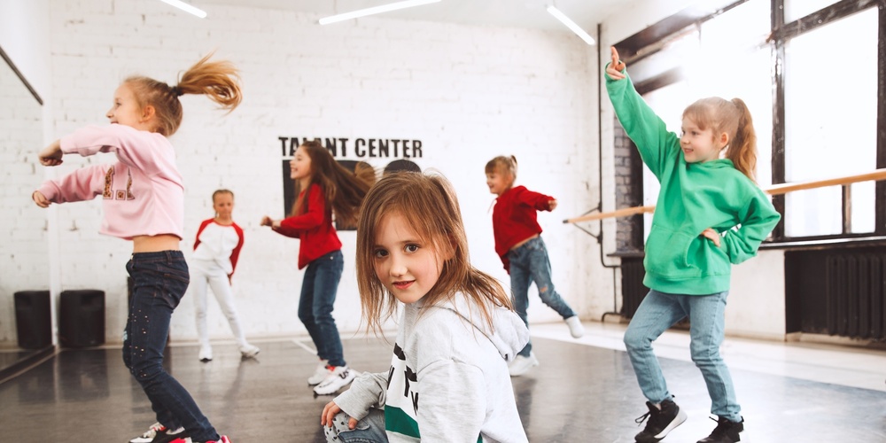 Barn dansar i en ljus dansstudio med stora fönster och spegelvägg.