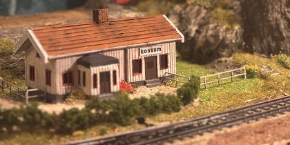 Modelljärnväg med ett litet hus, järnvägsspår och berg i bakgrunden.