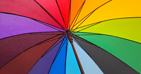 Närbild av en färgglad regnbågsfärgad paraply med vattendroppar på tyget.