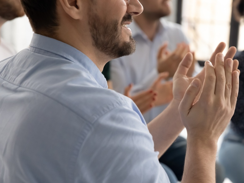 Flera personer sitter i en grupp och applåderar, fokus på händer och överkroppar.