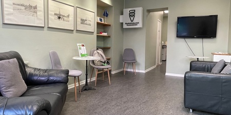 Väntrum med svarta soffor, grå stolar, konst på väggarna och en TV. Ljust och modernt inrett.