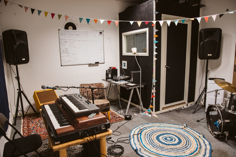 Ett musikrum med keyboard, trumset, högtalare, skrivbord och färgglada vimplar i taket.