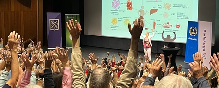 Föreläsning om fysisk aktivitet, hälsa och åldrande. Publik med händerna uppsträckta framför scenen.