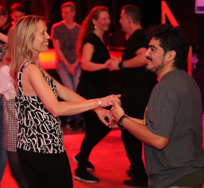 Två personer dansar tillsammans på ett dansgolv med andra par i bakgrunden.