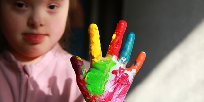 Ett barn visar sin hand täckt av färgglad fingerfärg, med ansiktet delvis synligt i bakgrunden.