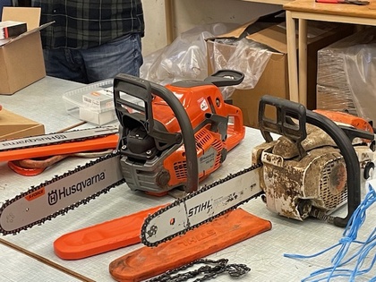 Två motorsågar av märkena Husqvarna och Stihl står på ett bord i en verkstadsmiljö.