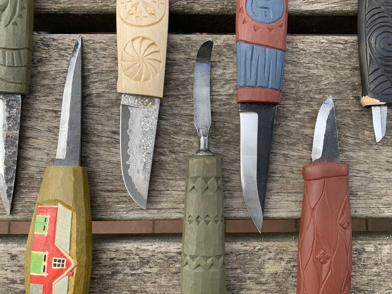 Flera handgjorda knivar med färgglada, snidade trähandtag ligger på en träyta.