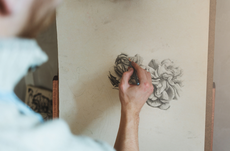 En person tecknar en blomma med blyertspenna på ett stort papper på ett staffli.