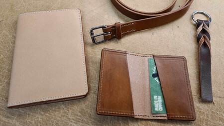Fyra läderprodukter: ett passfodral, ett bälte, en korthållare och en nyckelring på ett bord.