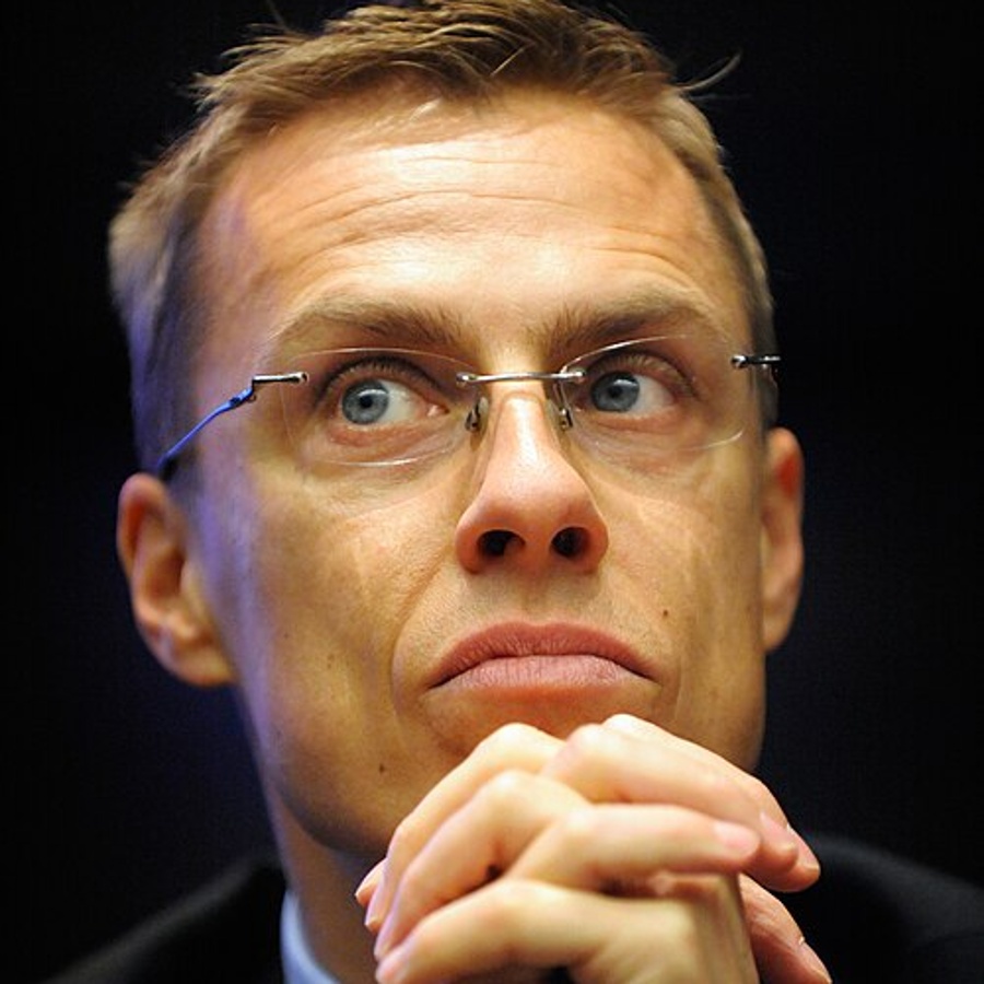 En person i kostym sitter med händerna knäppta framför sig vid ett bord med vattenflaskor.