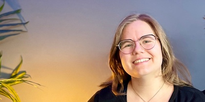 Två leende personer sitter tillsammans i en blå soffa i ett rum med blå vägg och grön växt.