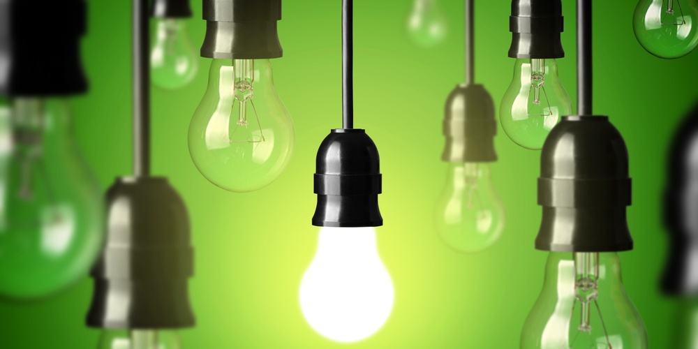 Flera hängande glödlampor mot grön bakgrund, en lampa lyser medan resten är släckta.