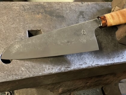 En stor kockkniv med trähandtag ligger på ett städ i en smedja.