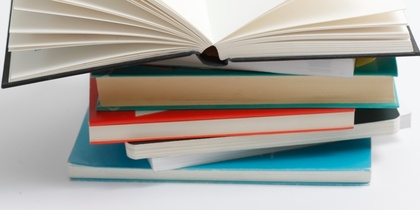 En hög med böcker där den översta boken är uppslagen och resten är stängda, mot vit bakgrund.