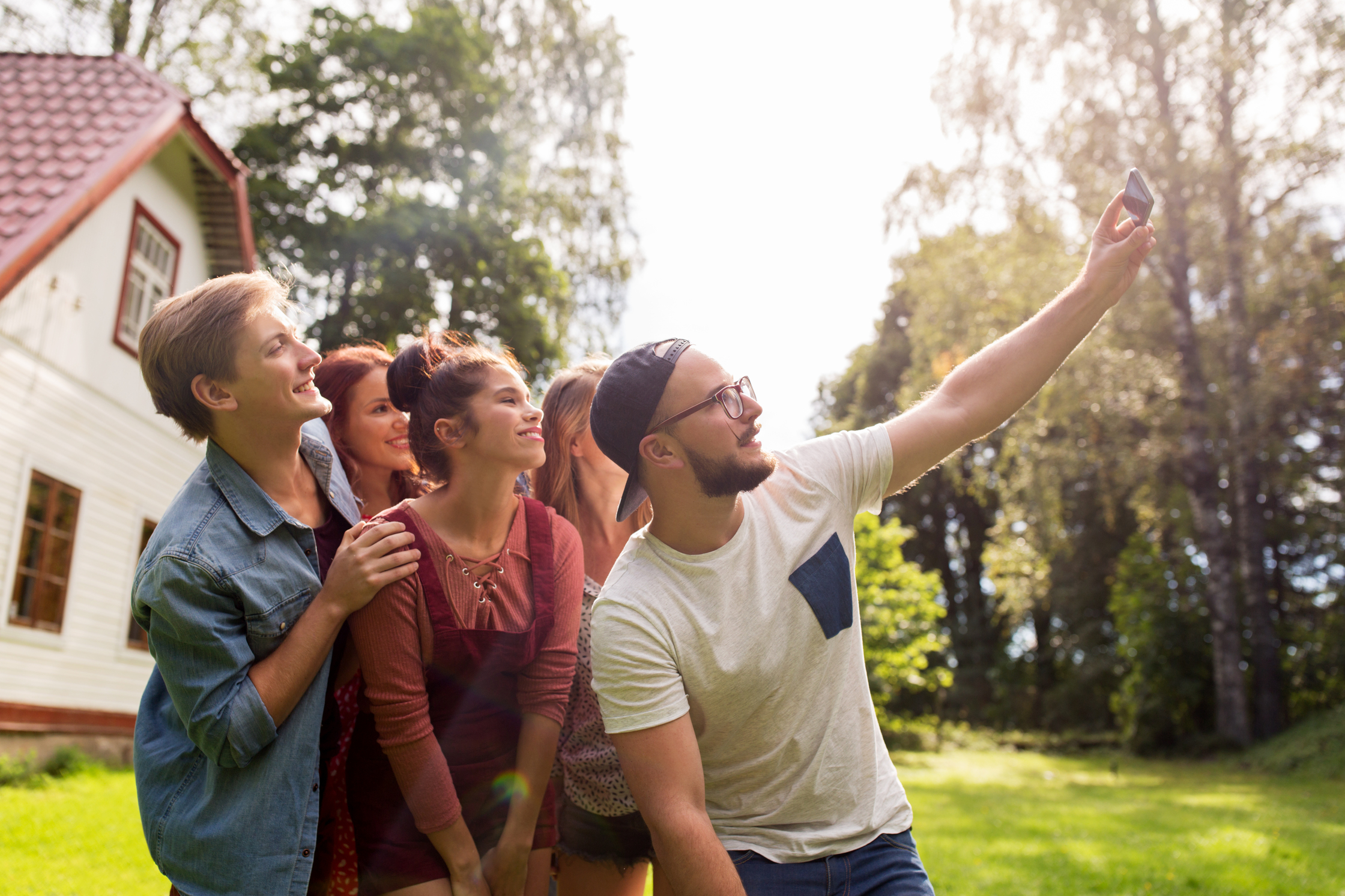 Fyra unga personer tar en selfie tillsammans utomhus vid ett hus en solig dag.