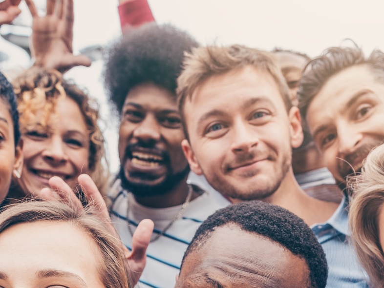 En grupp glada unga vuxna står tätt tillsammans och ler mot kameran utomhus.