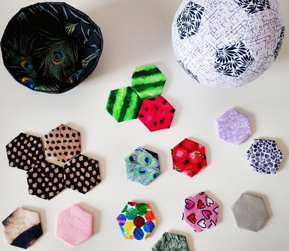 Färgglada tygbitar i hexagonform, en tygskål och en tygboll på ett vitt bord.