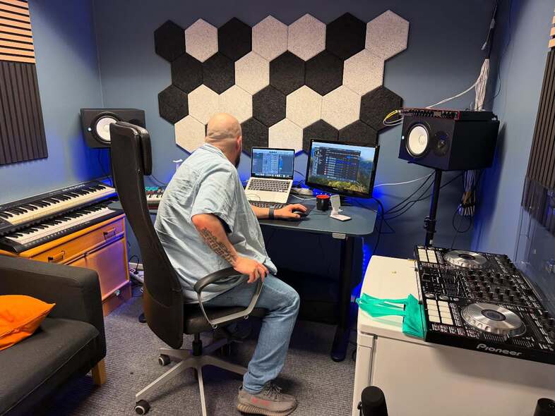 En person sitter vid ett skrivbord i en musikstudio med datorer, högtalare och musikutrustning.