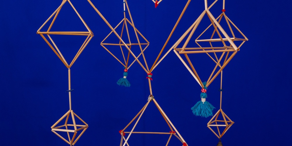 Himmelikrona av halm med dekorationer i blått garn, mot en knallblå bakgrund.