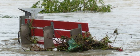 En röd parkbänk är delvis täckt av vatten och grenar efter en översvämning.