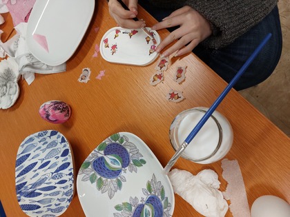 Person dekorerar porslin med decoupage och små figurer på ett träbord.