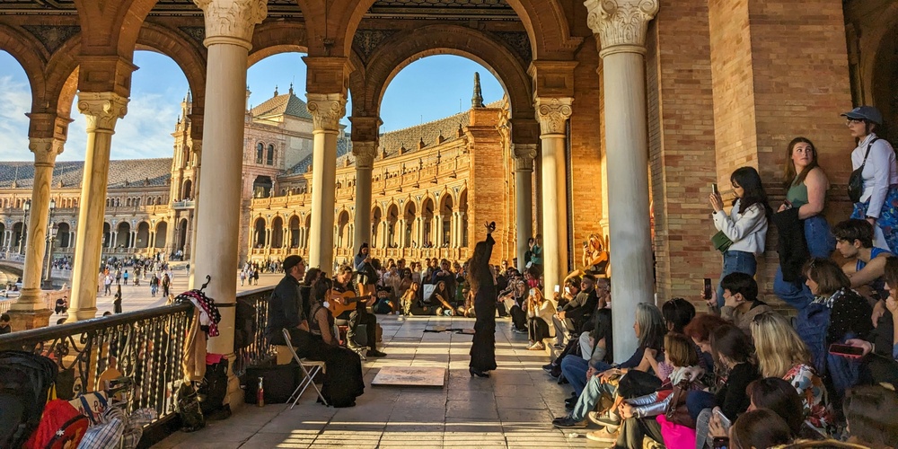 En flamencodansare uppträder inför en publik under valv på Plaza de España i Sevilla, med soligt väder utomhus.