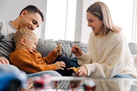 En familj med två vuxna och ett barn leker tillsammans med leksaksdjur i soffan och skrattar.
