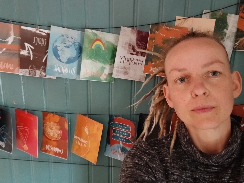 Person med blont hår i dreadlocks framför en vägg med färgglada kort upphängda på snören.