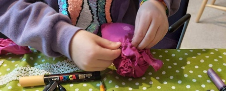 Barn pysslar vid ett bord med grönt prickigt tyg, pennor och tygbitar.