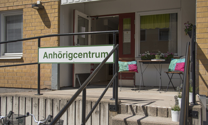 Entré till Anhörigcentrum med ramp, skylt och två stolar med färgglada kuddar utanför dörren.