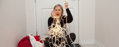 Kvinna sitter på golvet framför en dörr och kämpar med en trasslig ljusslinga, ser frustrerad ut.