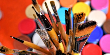 Flera olika penslar i en burk med färgglada färgburkar i bakgrunden.