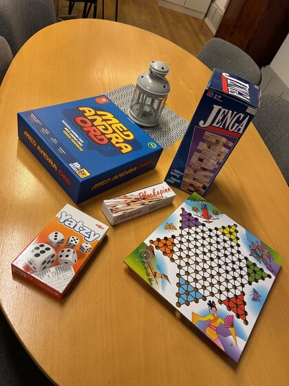 Ett bord med fem sällskapsspel, en ljuslykta och stolar runtom.