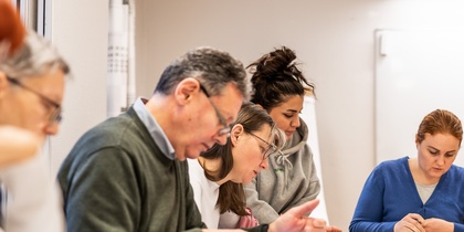 En grupp vuxna sitter vid ett bord och studerar tillsammans i ett klassrum.