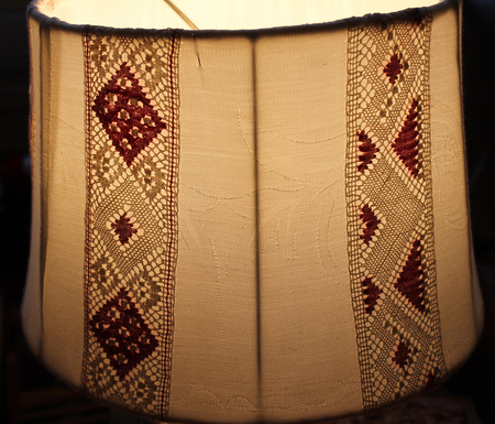 Närbild av en lampskärm med broderade och virkade mönster i beige och vinrött.