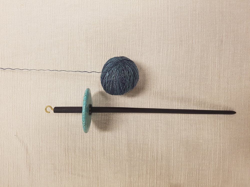 En slända och ett nystan av blått garn ligger på ett ljust underlag.