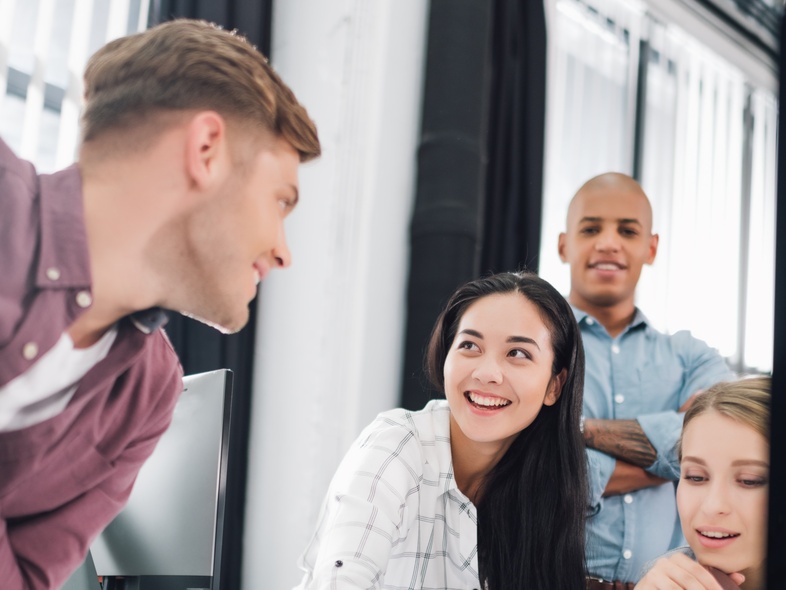 Fyra unga vuxna samarbetar och diskuterar vid ett skrivbord på ett modernt kontor.