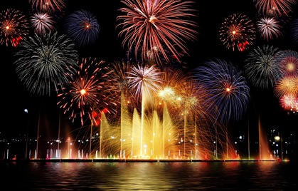 Färgglada fyrverkerier och fontäner lyser upp natthimlen över en sjö.