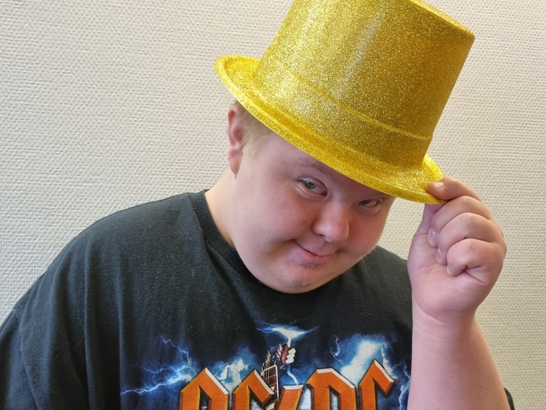 Person med svart AC/DC-tröja och glittrig gul hatt håller hatten med ena handen. Ansiktet är dolt.