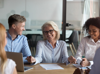 Fyra personer sitter runt ett bord på ett kontor och har ett glatt möte.