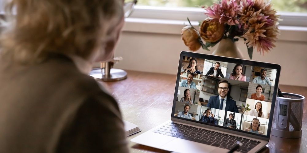 En person deltar i ett videomöte med flera deltagare på en bärbar dator vid ett skrivbord.